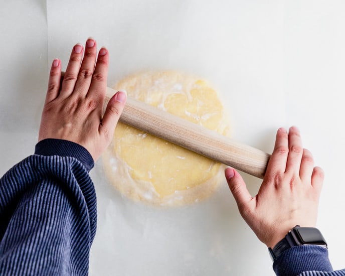 rolling the dough pastry using a wooden roller. 