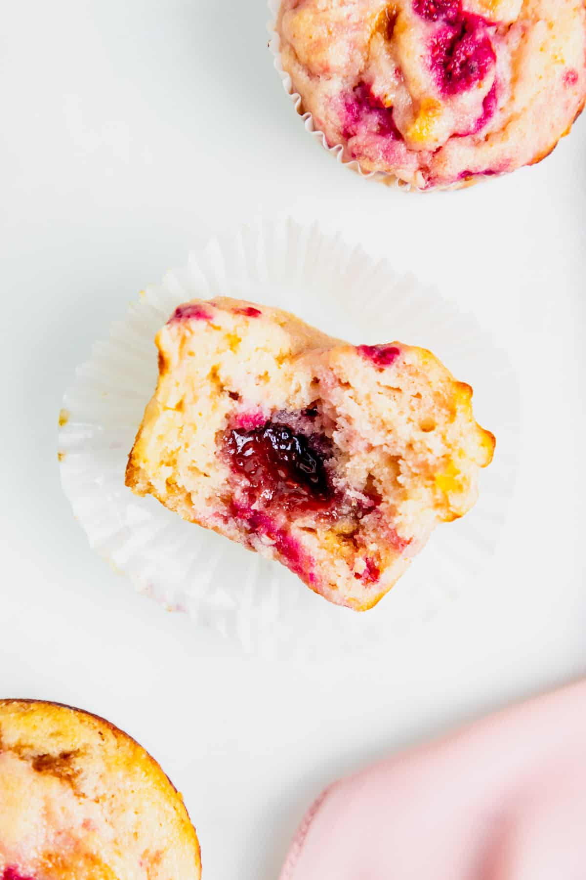 a gluten free raspberry muffin half eaten with raspberry jam in the middle