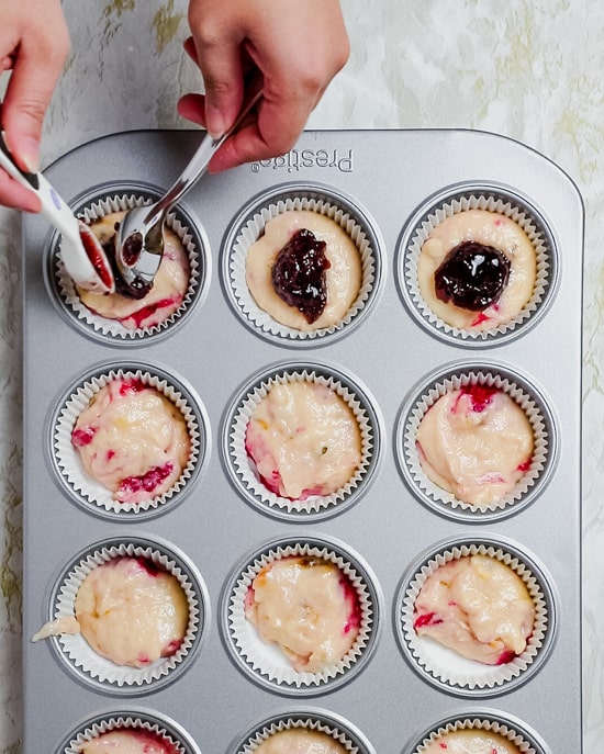 adding raspberry jam to the center of the gluten free raspberry muffins using a spoon