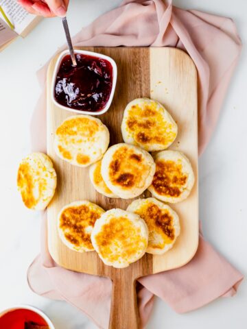 gluten free english muffins on a wooden serving board with a bowl of jam
