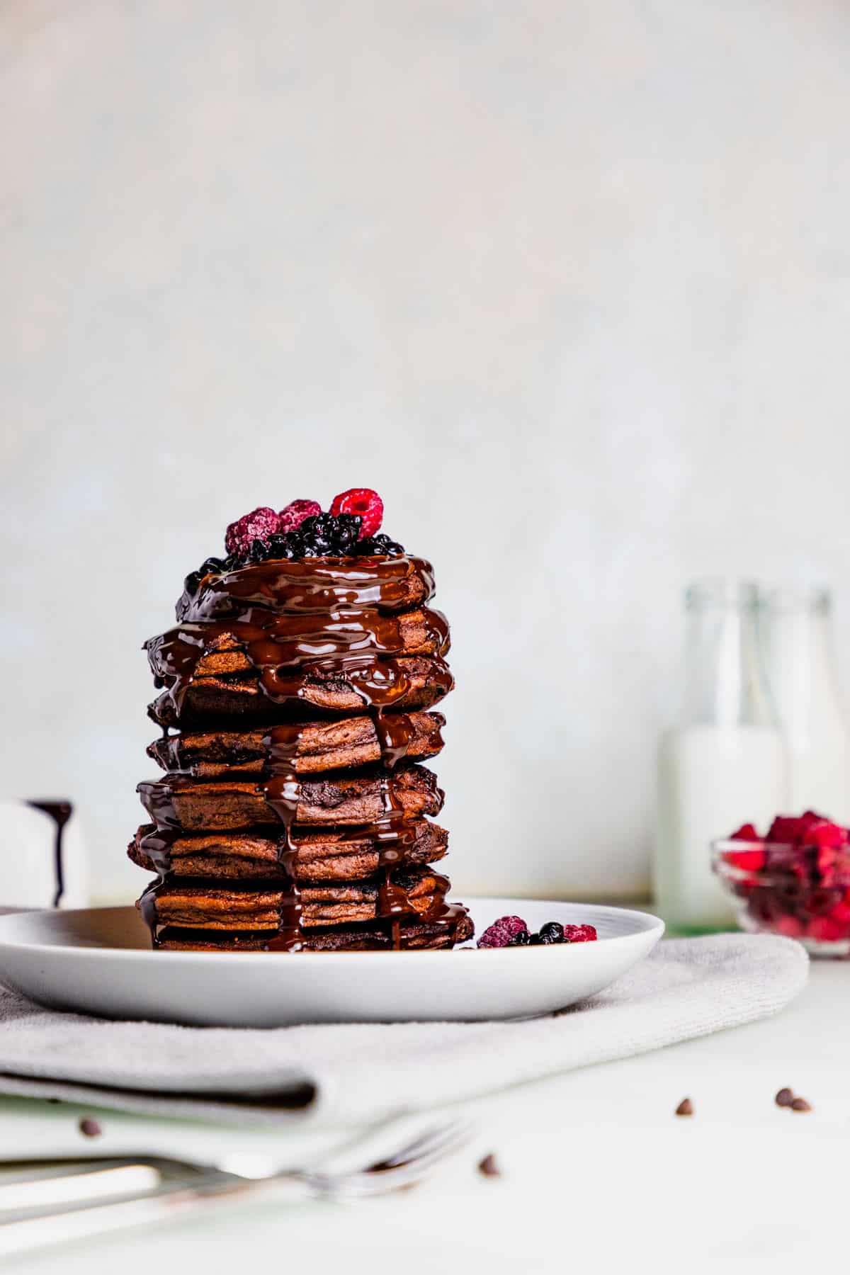chocolate pancakes stacked on top of each other, topped with chocolate ganache and fresh berries.
