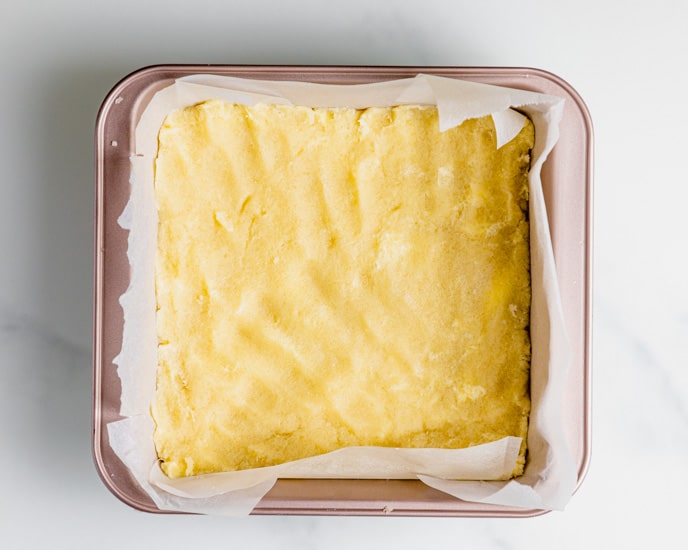 the gluten free pie crust in a square baking tin aligned with parchment paper. The crust is firmly pressed and is ready to be baked. 