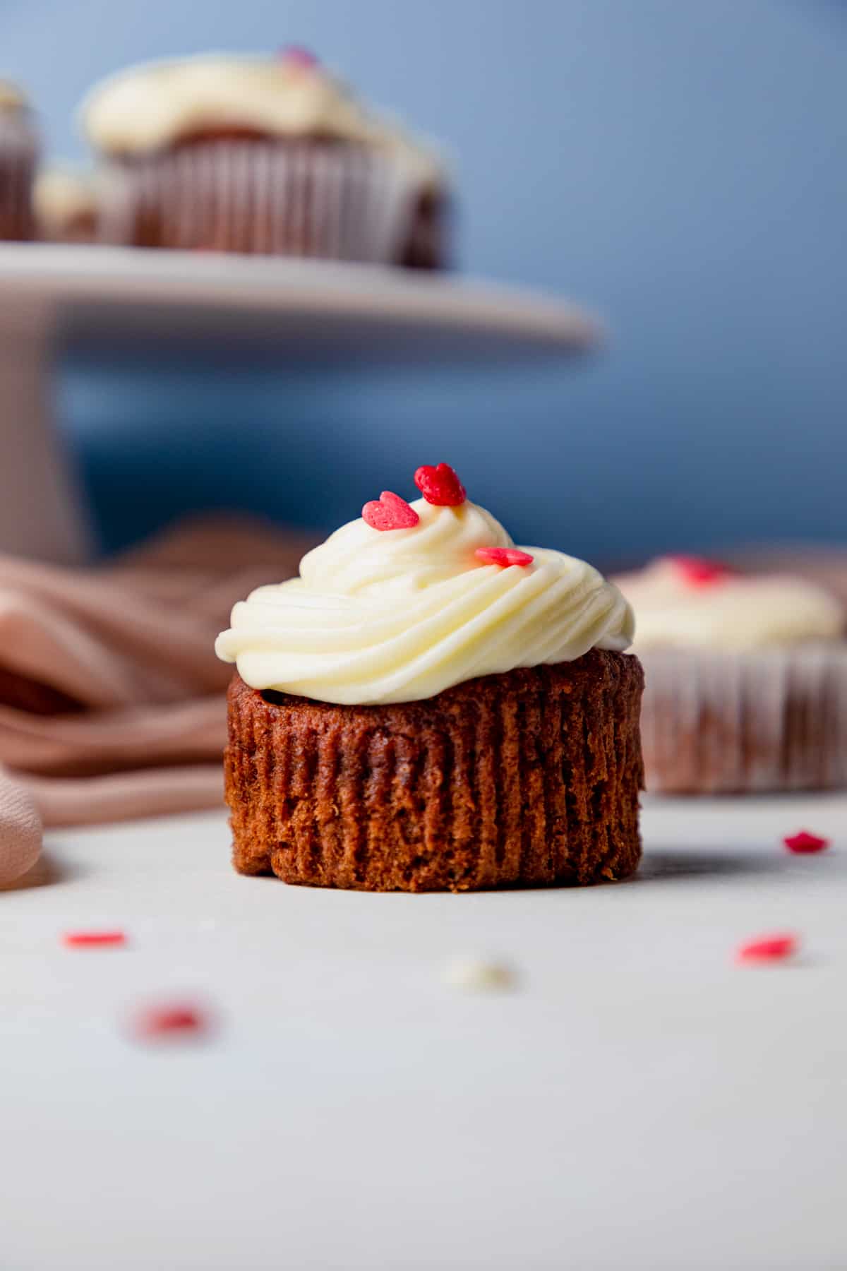gluten free red velvet cupcake with cream cheese frosting, and heart sprinkles on a white table. 
