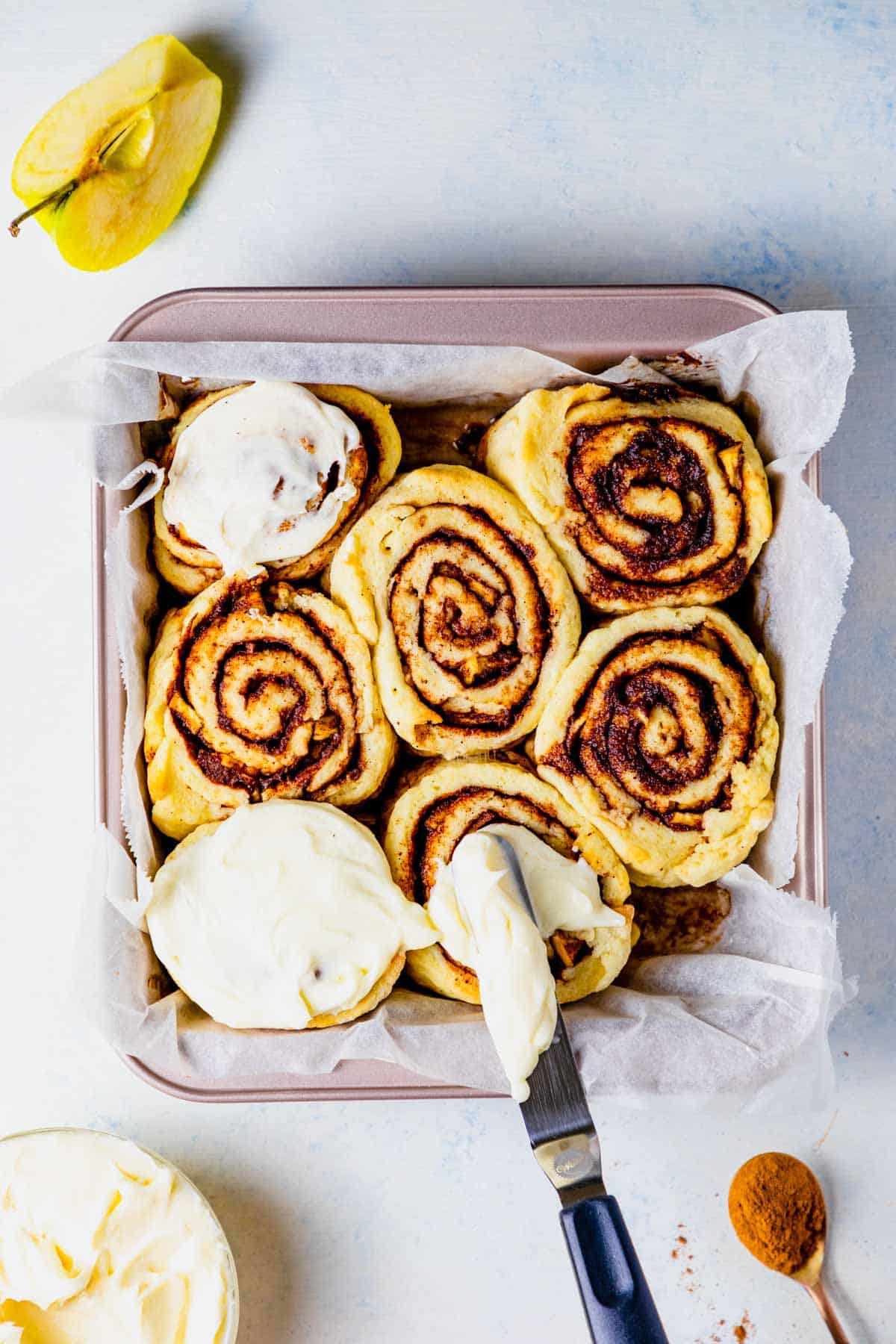 Cinnamon rolls with apple pie fillings being frosted with cream cheese frosting.