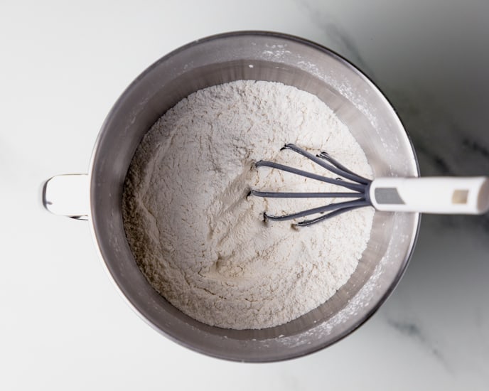 Dry ingredients in a stainless steel bowl with a gray whisk. 