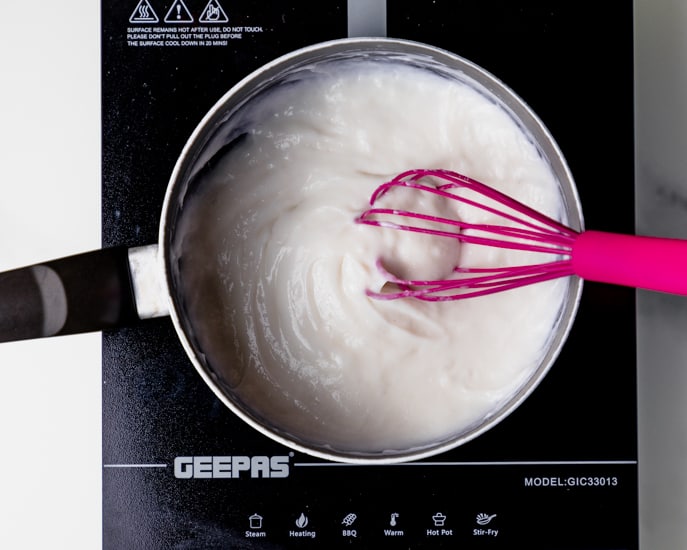 Tangzhong mixture is thick and slurry in a medium-sized saucepan, with a pink whisk. 