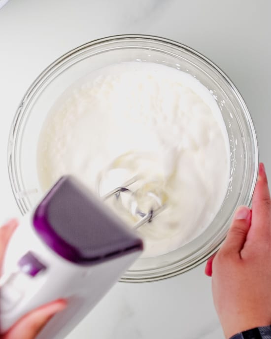 A handheld blender is being used to beat the heavy cream.