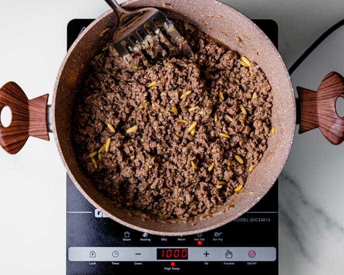 The ground beef filling with pine nuts in a cooking pot over medium heat.