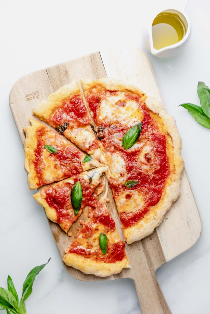 stretchy gluten free pizza placed on a wooden board surrounded by basil leaves. 